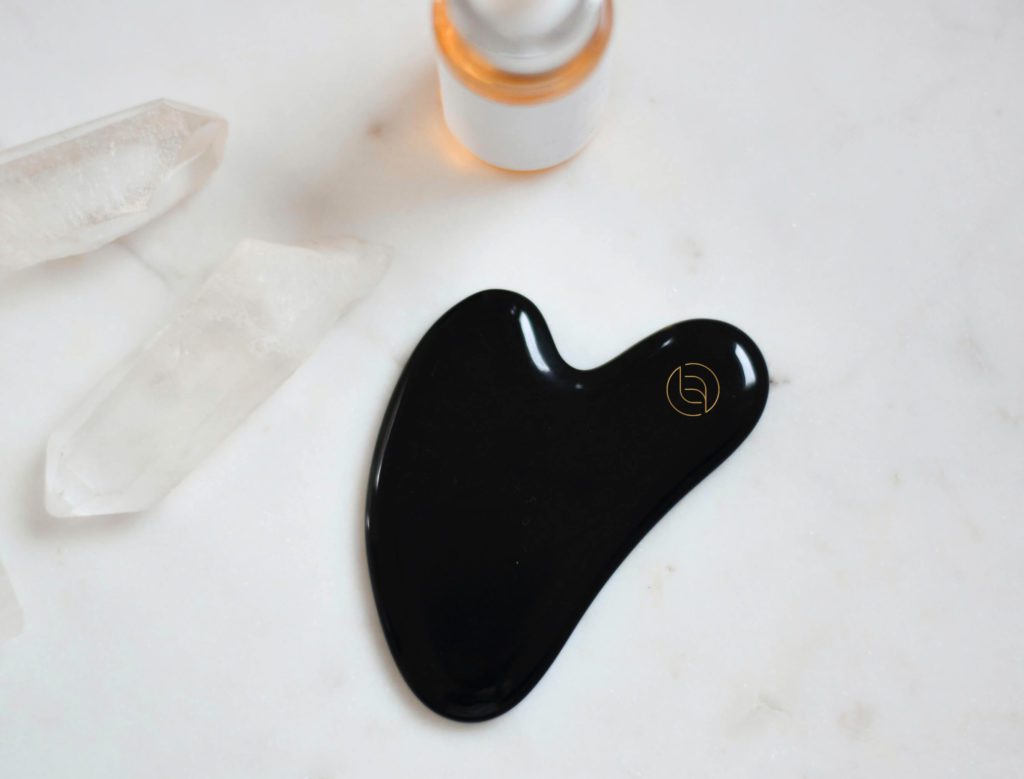A black Gua Sha tool with the brand mark etched into it